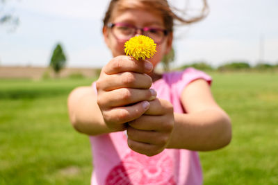 Midsection of girl holding pink flower on field