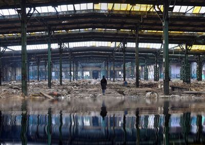 Rear view of woman reflecting on water under abandoned roof