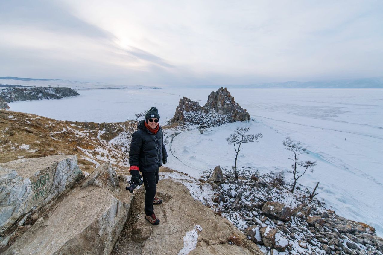 winter, leisure activity, sky, real people, beauty in nature, cold temperature, lifestyles, full length, one person, scenics - nature, snow, standing, cloud - sky, rock - object, rock, nature, non-urban scene, front view, warm clothing, outdoors