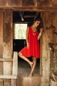 Full length of young woman in red dress standing at abandoned house