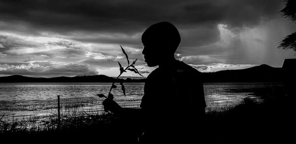 Silhouette man fishing in lake against sky during sunset