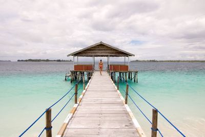 Rear view of woman walking on pier over sea against sky