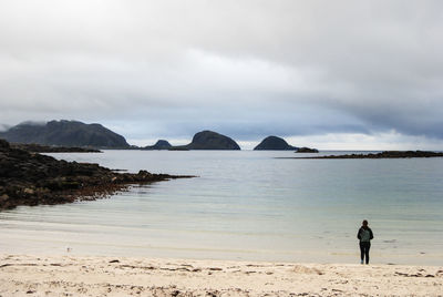 Rear view of woman standing on shore while looking at sea against cloudy sky