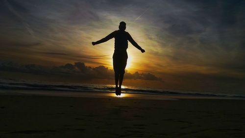 Silhouette woman standing on beach against sky during sunset