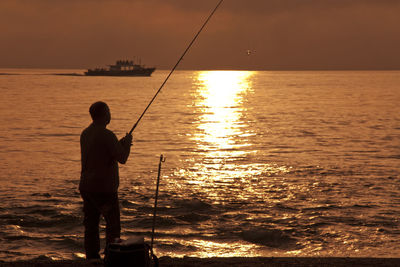 Rear view of silhouette man fishing in sea