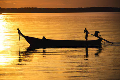 Silhouette man on boat in lake against sky during sunset