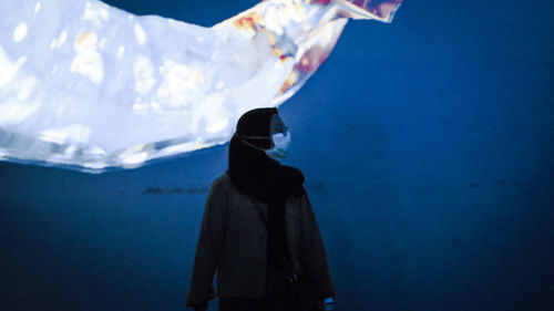 Side view of woman standing against blue wall