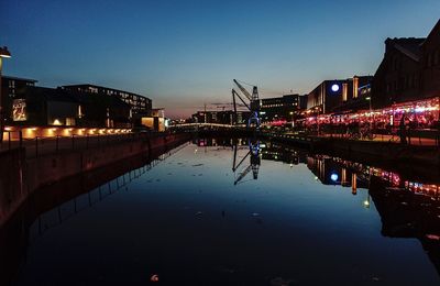 Illuminated buildings by river against sky at night