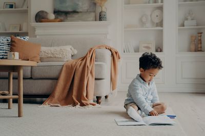 Rear view of boy looking at book at home