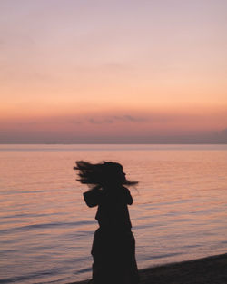 Silhouette woman standing at beach against sky during sunset