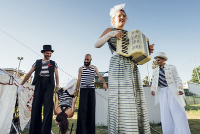 Female artist playing accordion while performers in background at circus