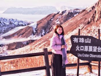 Portrait of young woman standing on railing against mountain