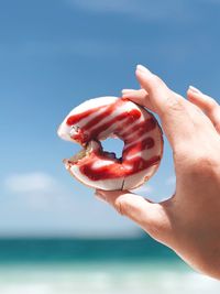 Cropped hand holding donut against sky