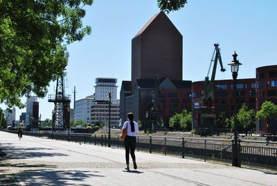 Rear view of man walking on street amidst buildings in city