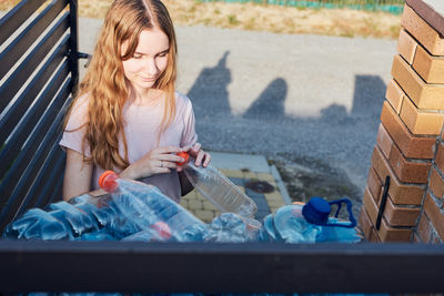 Young woman throwing out empty used plastic water bottles into trash bin. collecting plastic waste