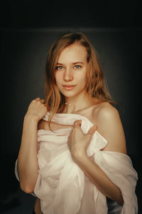 Portrait of young woman standing against black background