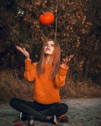 Full length of young woman holding pumpkin sitting against trees