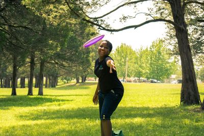 Portrait of young woman throwing plastic disc while standing on grassy field at park