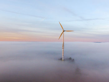 Windmills on shore against sky during sunset