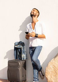 Full length of young man using phone while standing against wall