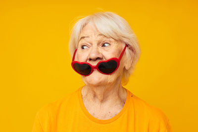 Senior woman wearing sunglasses against yellow background