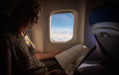 Mature female passenger reading magazine while sitting in airplane