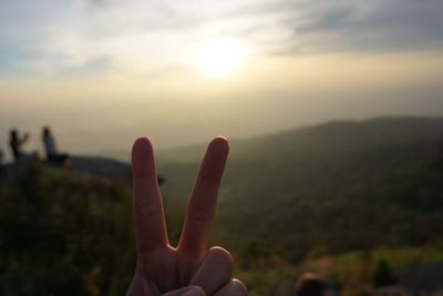 Close-up of hand against sky during sunset