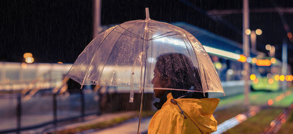 Side view of woman standing with umbrella in city at night