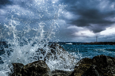 Sea waves splashing on rocks against sky