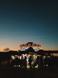 People at amusement park against clear sky at night