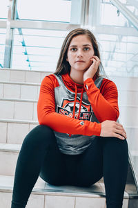 Portrait of young woman sitting on chair against wall