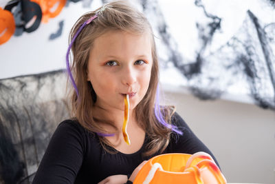 Little girl in costume of witch holding pumpkin jack with candies, celebrating halloween at home