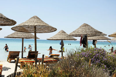 Thatched roofs at beach against clear sky