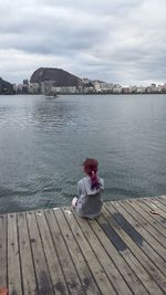 Rear view of woman sitting on shore against sky