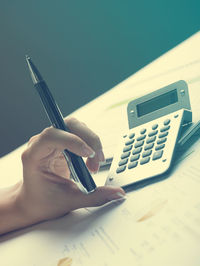 Cropped hands of businesswoman using calculator with documents at desk