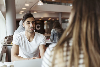 Smiling man discussing with female friend while studying in high school