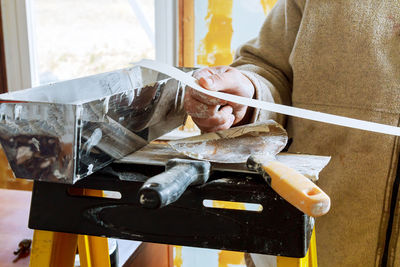 Midsection of man with paper and cement on ladder at home