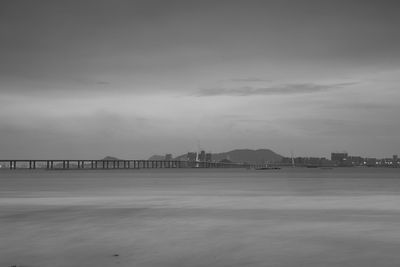 View of suspension bridge over sea against cloudy sky