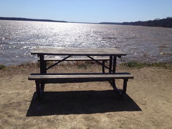 Empty bench by sea against clear sky