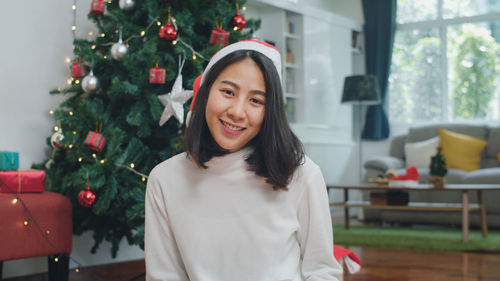 Portrait of happy young woman with christmas tree at home