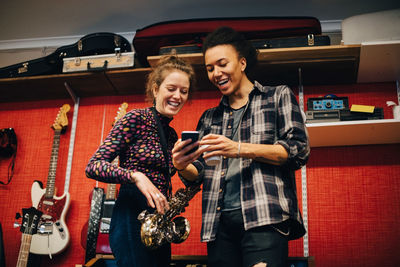 Woman with saxophone looking at man using smart phone while practicing at recording studio