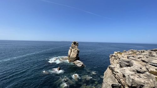 Rocks in sea against clear blue sky