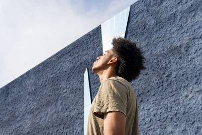 Low angle side view of peaceful african american male with afro hair standing under sunlight with closed eyes