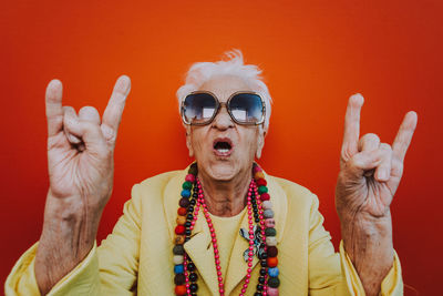 Portrait of senior woman wearing colorful jewelry and sunglasses against red background