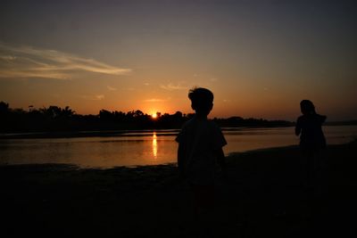 Silhouette people on beach against sky during sunset