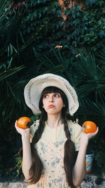 Portrait of young woman wearing hat standing against plants