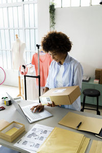 Female fashion designer using laptop while holding package in studio