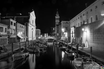 Boats moored in canal amidst buildings in city at night