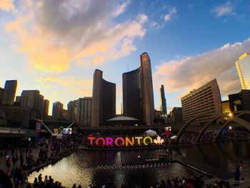 People at illuminated city against sky during sunset