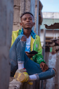 Portrait of young man sitting outdoors holding a mobile phone 